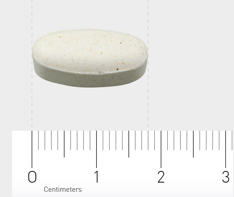 Eine weiße, ovale Tablette liegt auf einem Lineal mit Zentimetermarkierungen. Die Tablette hat kleine braune Sprenkel und liegt bei etwa 1,5 cm auf dem Lineal.