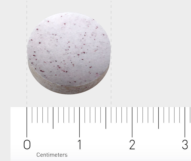 Das Bild zeigt eine runde, weiße Tablette mit kleinen roten Sprenkeln. Die Tablette liegt auf einem weißen Hintergrund, und darunter ist ein Lineal in Zentimetern zu sehen, das die Größe der Tablette anzeigt.