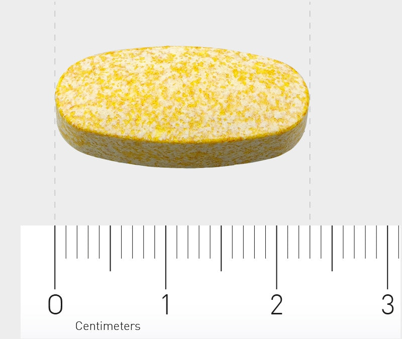 Eine gelb-weiße, ovale Tablette liegt auf einem Lineal, das in Zentimetern skaliert ist. Die Tablette misst etwa 2 Zentimeter in der Länge. Der Hintergrund ist grau.