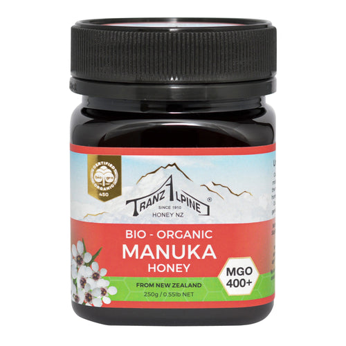 Ein Glas Bio-Manuka-Honig der Marke TranzAlpine ist abgebildet. Das Etikett zeigt ein Bergmotiv und die Aufschrift 'Bio-Organic Manuka Honey MGO 400+ aus Neuseeland'. Der Honig ist in einem dunklen Glas mit schwarzem Deckel verpackt.