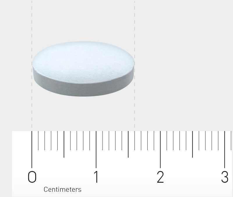 Eine weiße, runde Tablette liegt auf einer grauen Oberfläche. Darunter befindet sich ein Lineal, das in Zentimetern skaliert ist. Die Tablette hat einen Durchmesser von etwa 1,5 Zentimetern.