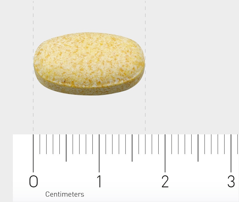 Das Bild zeigt eine ovale, gelbliche Tablette, die auf einem Lineal mit Zentimeter-Markierungen liegt. Die Tablette ist etwa 1,5 cm lang. Der Hintergrund ist grau.