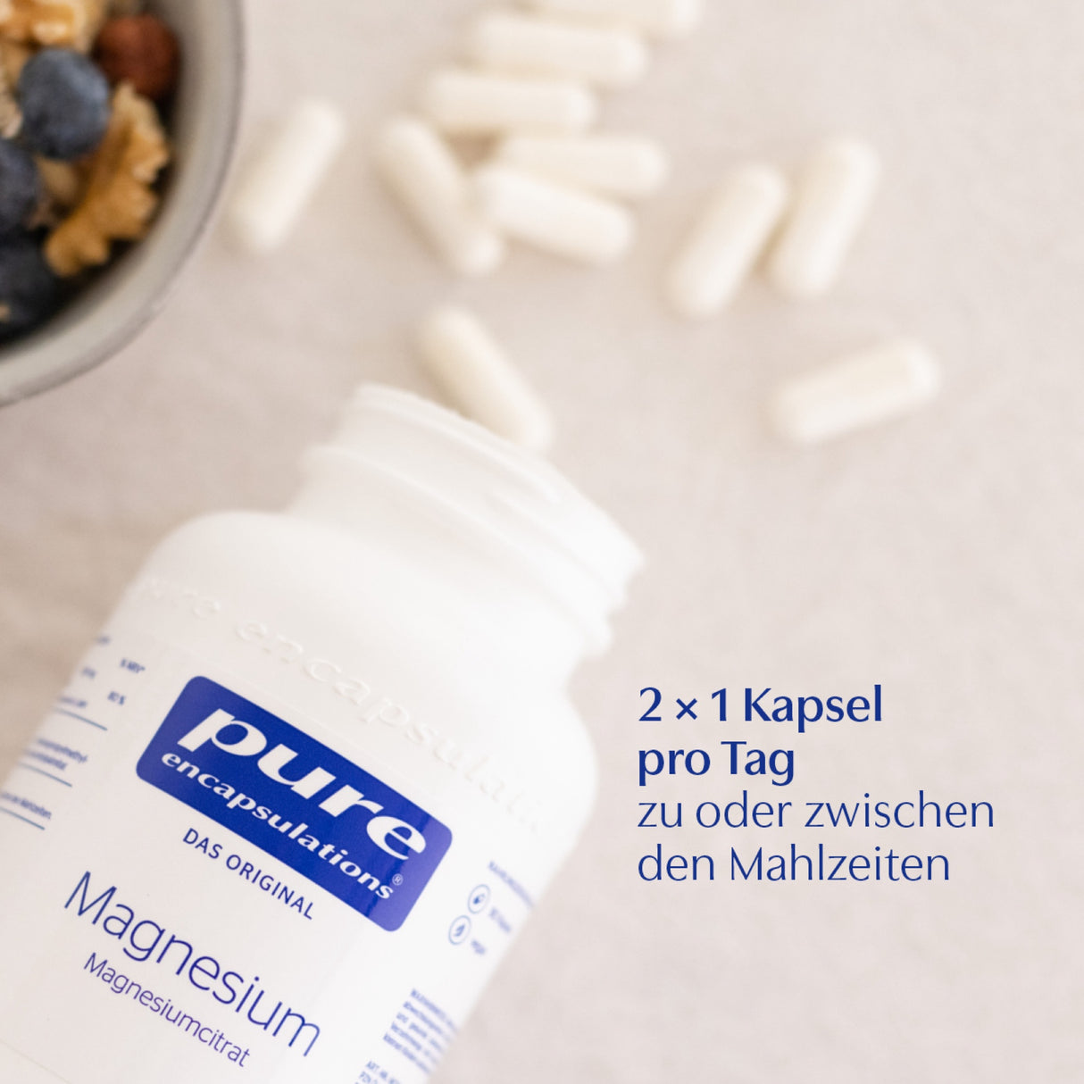 Das Bild zeigt eine offene Flasche Magnesiumcitrat-Kapseln der Marke 'pure encapsulations' auf einer hellen Oberfläche, umgeben von verstreuten Kapseln. Links oben ist eine Schale mit Beeren zu sehen. Auf dem Bild steht der Text: '2 × 1 Kapsel pro Tag zu oder zwischen den Mahlzeiten'.