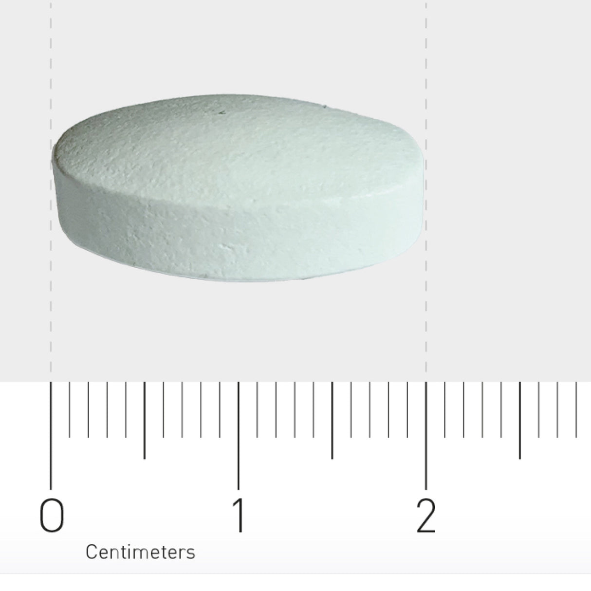 Eine weiße, runde Tablette liegt auf einem Lineal mit Zentimeterangaben. Die Tablette ist etwa 1,5 Zentimeter groß.