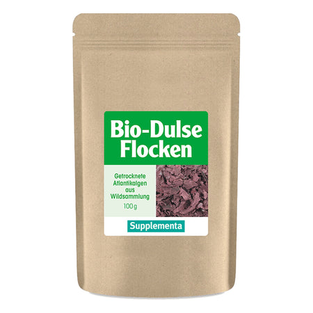 Eine braune Verpackungstüte mit einem grünen Etikett, auf dem 'Bio-Dulse Flocken' steht. Darunter befindet sich die Beschreibung 'Getrocknete Atlantikalgen aus Wildsammlung 100g' und das Logo 'Supplementa'.