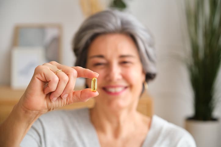 Senior woman holding fish oil supplement at home