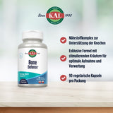 Das Bild zeigt eine Verpackung des Nahrungsergänzungsmittels 'KAL Bone Defense' auf einem Tisch. Links ist eine weiße Flasche mit Etikett zu sehen, das die Marke und den Produktnamen zeigt. Rechts sind drei Aufzählungspunkte mit Informationen über das Produkt: 1. Nährstoffkomplex zur Unterstützung der Knochen, 2. Exklusive Formel mit stimulierenden Kräutern für optimale Aufnahme und Verwertung, 3. 90 vegetarische Kapseln pro Packung. Im Hintergrund ist ein unscharfer grüner Bereich zu erkennen.