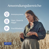 Eine Frau steht in einem Feld und hält einen Grashalm. Sie trägt eine Brille und ein dunkelgrünes Hemd. Links im Bild sind Symbole mit den Texten 'Immunsystem', 'Haut, Haare & Nägel' und 'Fruchtbarkeit' zu sehen. Am unteren Rand befindet sich das Logo von 'pure encapsulations'. Der Himmel ist klar und blau.