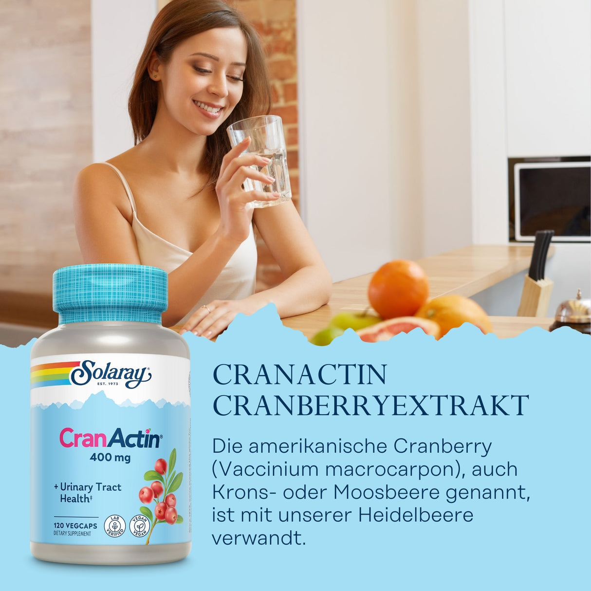 Eine Frau in einem weißen Top sitzt an einem Küchentresen und hält ein Glas Wasser. Auf dem Tresen liegen Früchte. Im Vordergrund ist eine Flasche Solaray CranActin Cranberryextrakt zu sehen. Der Hintergrund zeigt eine moderne Küche mit Backsteinwand.