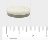 Eine weiße, ovale Tablette liegt auf einem Lineal mit Zentimetermarkierungen. Die Tablette hat kleine braune Sprenkel und liegt bei etwa 1,5 cm auf dem Lineal.