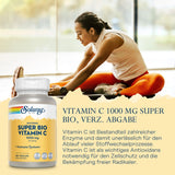 Eine Frau in Sportkleidung dehnt sich auf einem Boden, während sie auf einem Bein sitzt. Sie trägt ein weißes Oberteil und orangefarbene Leggings. Neben ihr ist eine Flasche Solaray Super Bio Vitamin C 1000 mg abgebildet. Der Hintergrund ist unscharf, möglicherweise ein Innenraum mit großen Fenstern. Auf der Flasche steht, dass Vitamin C wichtig für das Immunsystem ist. Der Text auf dem Bild beschreibt die Vorteile von Vitamin C als Antioxidans und seine Rolle in Stoffwechselprozessen.