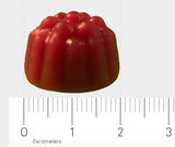 Ein rotes, gummiartiges Süßwarenstück in Form eines Fruchtgummis liegt auf einem weißen Hintergrund. Darunter ist ein Lineal mit Zentimeter-Markierungen zu sehen, das die Größe des Fruchtgummis mit etwa 2 cm Durchmesser anzeigt.