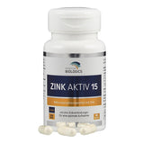 Eine weiße Plastikflasche mit dem Etikett 'Zink Aktiv 15' von American Biologics. Die Flasche enthält Nahrungsergänzungsmittel mit Zink. Auf dem Etikett sind Informationen über die Inhaltsstoffe und Hinweise wie 'Vegan' und 'Non GMO' abgebildet. Vor der Flasche liegen mehrere weiße Kapseln.