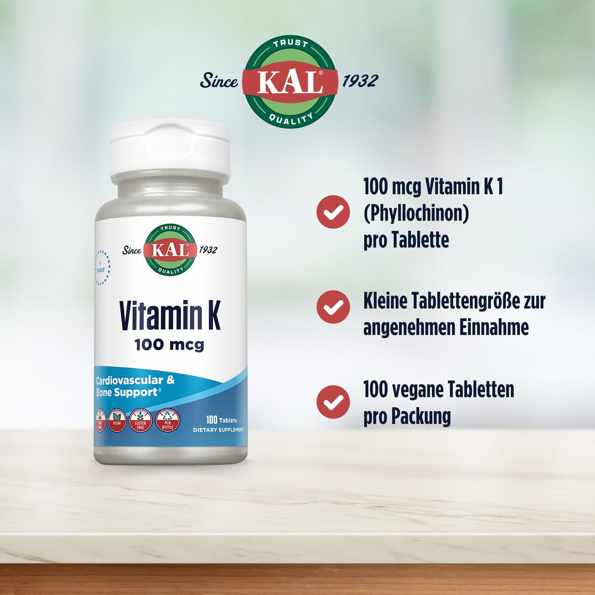 Das Bild zeigt eine Verpackung von KAL Vitamin K 100 mcg auf einem Tisch. Links ist die Flasche mit dem Logo „KAL Since 1932“ zu sehen. Rechts sind drei Vorteile aufgelistet: 100 mcg Vitamin K1 pro Tablette, kleine Tablettengröße und 100 vegane Tabletten pro Packung. Der Hintergrund ist unscharf und hell.