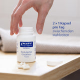 Eine Hand greift nach einem geöffneten weißen Fläschchen mit der Aufschrift 'pure encapsulations Reduziertes Glutathion'. Daneben liegen weiße Kapseln auf einem Holztisch. Im Hintergrund ist ein Handtuch zu sehen. Der Text '2 × 1 Kapsel pro Tag zwischen den Mahlzeiten' steht rechts im Bild.