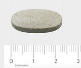 Eine ovale, graue Tablette liegt auf einer weißen Oberfläche. Darunter befindet sich ein Lineal mit Zentimeter-Markierungen, das die Länge der Tablette anzeigt. Die Tablette ist etwa 2,5 cm lang.
