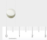 Ein kleines, rundes, weißes Objekt, das wie eine Tablette aussieht, liegt auf einer weißen Oberfläche. Unterhalb des Objekts ist ein Lineal mit Zentimeter-Markierungen zu sehen, das die Größe des Objekts zeigt. Der Hintergrund ist einheitlich hellgrau.