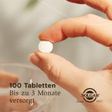 Nahaufnahme einer Hand, die eine weiße Tablette hält. Im Hintergrund ist ein Glas zu sehen. Text auf dem Bild: '100 Tabletten, Bis zu 3 Monate versorgt'. Logo: Solgar, Since 1947.