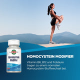 Eine Frau in Sportkleidung steht auf einem Berggipfel und dehnt ihr Bein. Im Vordergrund ist eine Flasche "Homocystein Modifier" von KAL zu sehen. Der Hintergrund zeigt eine Berglandschaft unter klarem Himmel. Text auf dem Bild beschreibt die Vorteile von Vitamin B6, B12 und Folsäure für den Homocystein-Stoffwechsel.