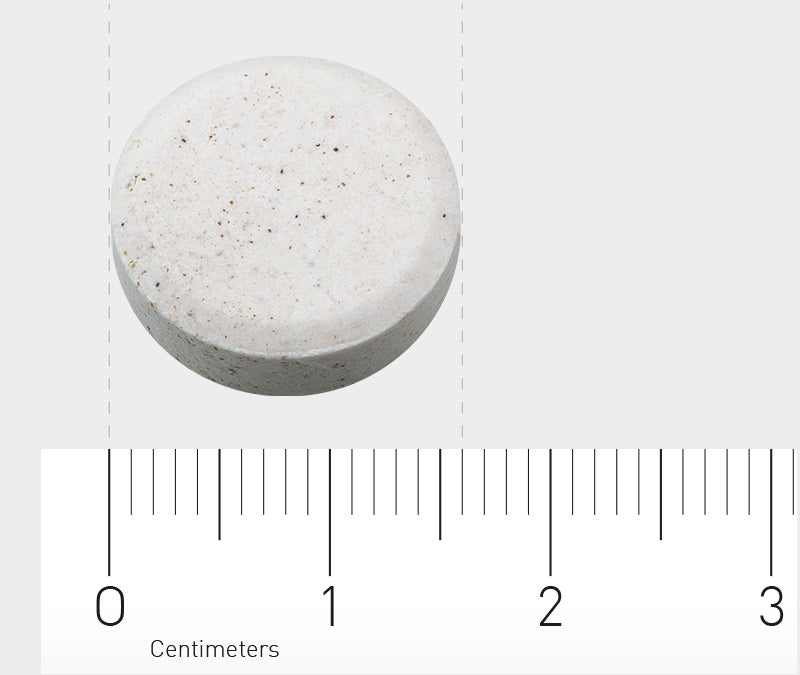 Eine runde, weiße Tablette liegt auf einer grauen Oberfläche. Unter der Tablette befindet sich ein Lineal, das in Zentimetern skaliert ist. Die Tablette hat einen Durchmesser von etwa 1,5 Zentimetern.