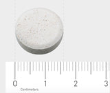 Eine runde, weiße Tablette liegt auf einer grauen Oberfläche. Unter der Tablette befindet sich ein Lineal, das in Zentimetern skaliert ist. Die Tablette hat einen Durchmesser von etwa 1,5 Zentimetern.