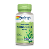 Das Bild zeigt eine Plastikflasche mit grüner Kappe, die Spirulina-Kapseln von Solaray enthält. Auf dem Etikett steht 'True Herbs Spirulina 410 mg', zusammen mit 'Herbal Support', '100 Vegcaps', und mehreren Prüfsiegeln. Die Flasche hat ein grünes Design mit Algen-Motiv.