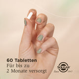 Eine Hand mit grün lackierten Nägeln hält eine weiße Tablette vor einem beigen Hintergrund. Auf dem Bild steht: '60 Tabletten, für bis zu 2 Monate versorgt'. Das Solgar-Logo ist unten rechts zu sehen.