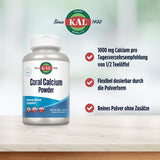 Das Bild zeigt eine Verpackung von KAL Coral Calcium Powder, einem Nahrungsergänzungsmittel. Die Verpackung ist weiß mit blauen Akzenten. Auf der rechten Seite des Bildes sind drei Vorteile des Produkts aufgelistet: 1000 mg Calcium pro Tagesverzehrsempfehlung von 1/2 Teelöffel, flexibel dosierbar durch die Pulverform und reines Pulver ohne Zusätze. Oben ist das KAL-Logo mit dem Schriftzug 'Since 1932' zu sehen. Der Hintergrund ist unscharf und in hellen, neutralen Farben gehalten.