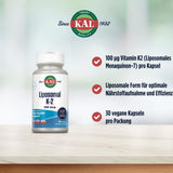 Das Bild zeigt eine Flasche KAL Liposomal K-2 Supplement auf einem Tisch. Die Flasche ist weiß mit einem Etikett, das den Produktnamen und die Dosierung von 100 mcg anzeigt. Daneben befinden sich drei Aufzählungspunkte: 100 µg Vitamin K2 (Liposomales Menaquinon-7) pro Kapsel, Liposomale Form für optimale Nährstoffaufnahme und Effizienz, 30 vegane Kapseln pro Packung. Im Hintergrund ist ein verschwommener, heller Hintergrund zu sehen. Das KAL-Logo ist oben links abgebildet mit dem Text "Since 1932".