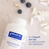Eine weiße Flasche mit der Aufschrift 'pure encapsulations Magnesium' liegt auf einem Tisch. Daneben liegen weiße Kapseln und einige Blaubeeren. Der Text '3 x 1 Kapsel pro Tag zu oder zwischen den Mahlzeiten' ist sichtbar.