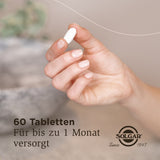 Eine Hand hält eine weiße Tablette. Im Hintergrund ist ein unscharfer, natürlicher Hintergrund zu sehen. Auf dem Bild steht: '60 Tabletten Für bis zu 1 Monat versorgt SOLGAR Since 1947'.