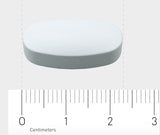 Eine weiße, ovale Tablette liegt auf einer grauen Oberfläche. Darunter befindet sich ein Lineal, das die Größe der Tablette in Zentimetern anzeigt. Die Tablette ist etwa 2 cm lang. Das Bild hat einen neutralen Hintergrund.