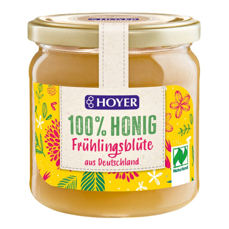 Ein Glas mit Hoyer 100% Honig, Frühlingsblüte, aus Deutschland. Buntes Etikett mit Blumenmotiven und Naturland-Logo.