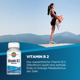 Eine Frau in Sportkleidung steht auf einem Bein auf einem Berg mit blauem Himmel im Hintergrund. Unten links ist eine Flasche Vitamin B2 abgebildet. Rechts daneben steht: "Vitamin B2 100 mg. Das wasserlösliche Vitamin B2 (Riboflavin) spielt eine zentrale Rolle im Energie-Metabolismus der Zelle."