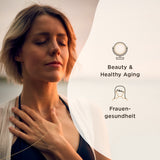 Eine Frau mit geschlossenen Augen steht im Freien, legt eine Hand auf ihre Brust. Rechts sind die Begriffe 'Beauty & Healthy Aging' und 'Frauengesundheit' neben passenden Symbolen abgebildet. Der Hintergrund ist unscharf und zeigt eine natürliche Umgebung.