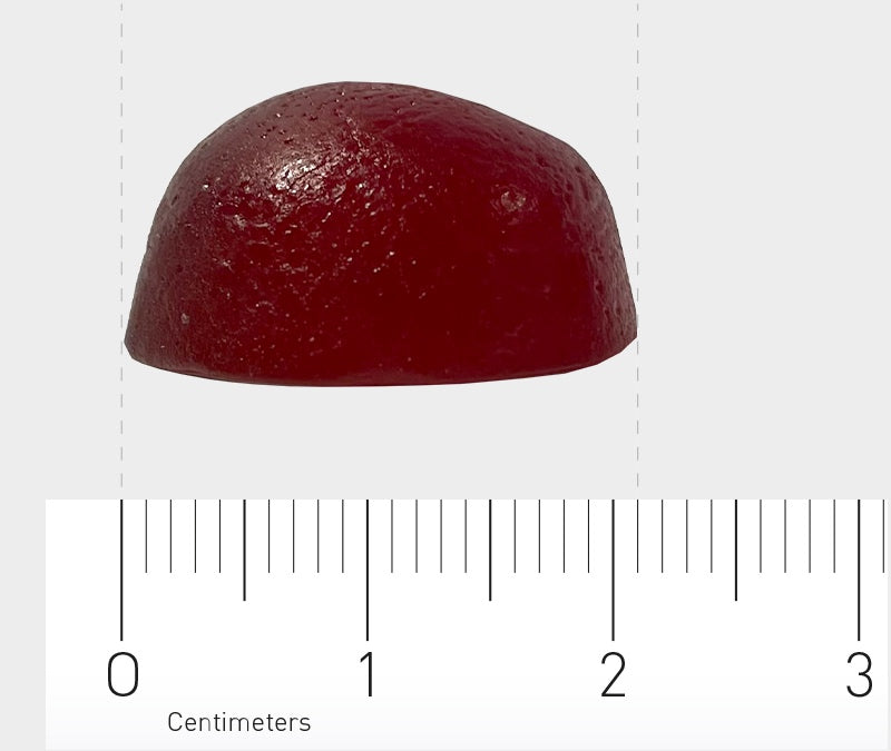 Das Bild zeigt ein halbkugelförmiges, dunkelrotes Objekt, das auf einem Lineal liegt. Das Lineal hat Markierungen in Zentimetern. Das Objekt sieht aus wie ein Gummibärchen oder Gelee. Der Hintergrund ist neutral, in einem hellen Grauton.