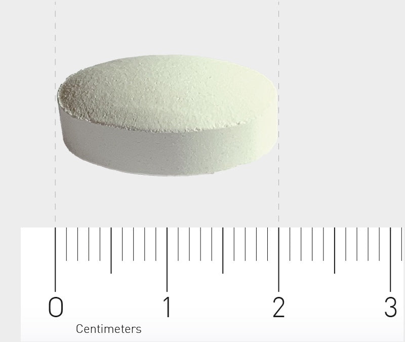Eine weiße Tablette liegt auf einem Lineal, das in Zentimetern skaliert ist. Die Tablette hat einen Durchmesser von etwa 1,5 cm. Der Hintergrund ist neutral grau.