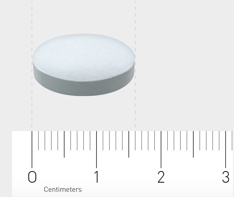 Eine weiße Tablette liegt auf einer hellgrauen Oberfläche. Darunter befindet sich ein Lineal, das in Zentimetern markiert ist. Die Tablette ist etwa 1,5 Zentimeter groß.