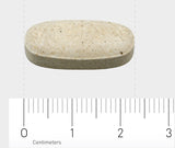Ein einzelnes ovales, cremefarbenes Tablett liegt auf einer grauen Oberfläche. Unter der Tablette befindet sich ein Lineal mit Zentimeter-Einteilungen, das die Größe der Tablette anzeigt. Die Tablette ist etwa 2,5 Zentimeter lang.