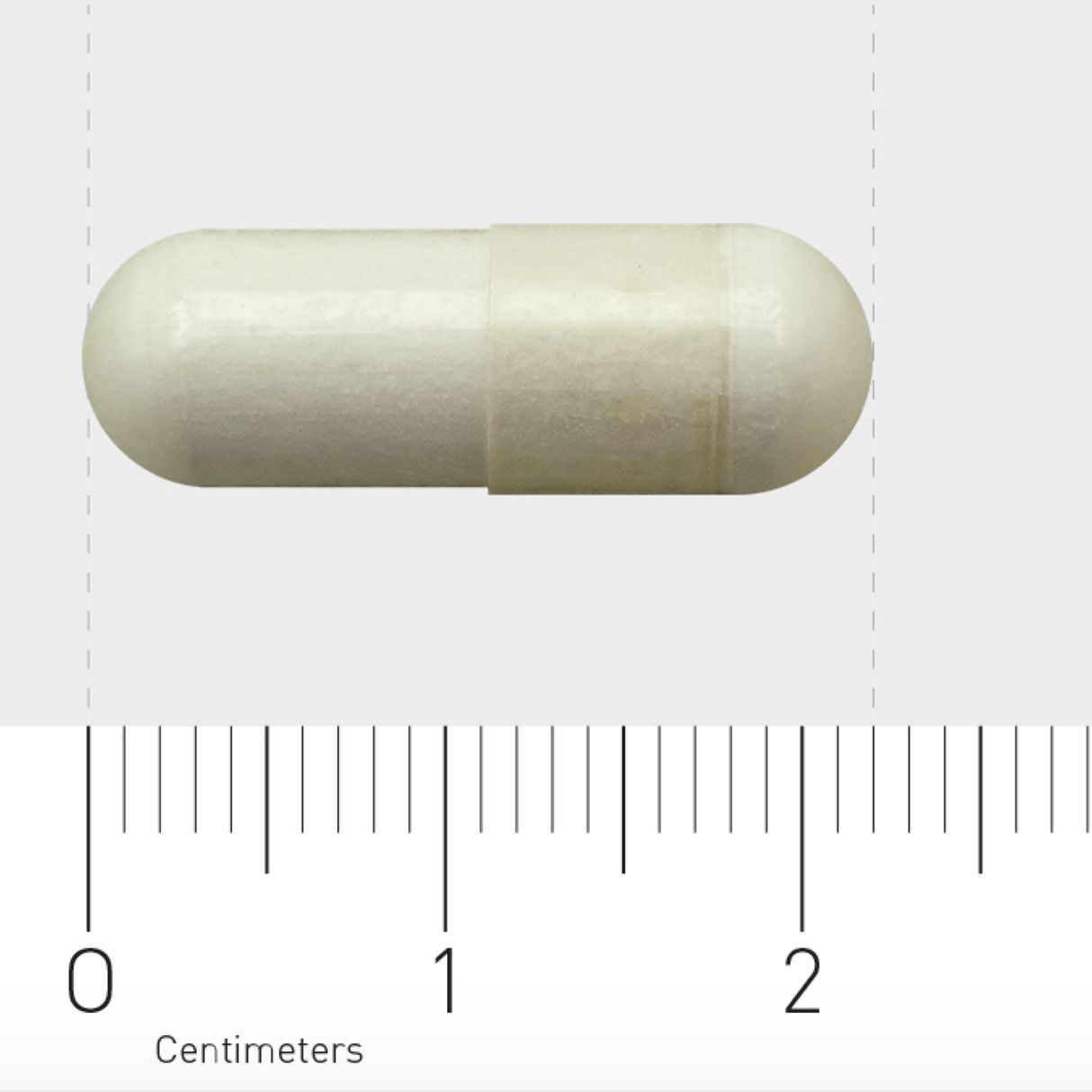 Eine weiße Kapsel liegt horizontal auf einem Lineal, das in Zentimetern skaliert ist. Die Kapsel ist etwa 2 Zentimeter lang.