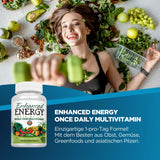 Frau liegt lächelnd auf Gemüse und Obst, hält grüne Hantel. Text über Multivitamin mit Obst, Gemüse, Greenfoods und Pilzen. Produktflasche sichtbar.