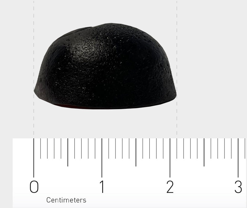 Ein schwarzes, kuppelförmiges Objekt liegt auf einer weißen Oberfläche. Darunter befindet sich ein Lineal, das in Zentimetern skaliert ist. Das Objekt hat einen Durchmesser von etwa 2 Zentimetern.