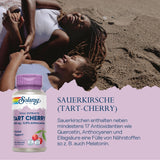 Zwei lachende Personen liegen am Strand. Eine Flasche Solaray Tart Cherry Nahrungsergänzungsmittel ist abgebildet. Text beschreibt die Vorteile von Sauerkirschen.