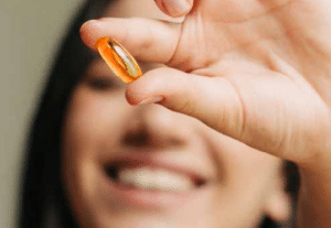 Frau hält eine Ölkapsel mit Omega-3-Fettsäuren zwischen den Fingern