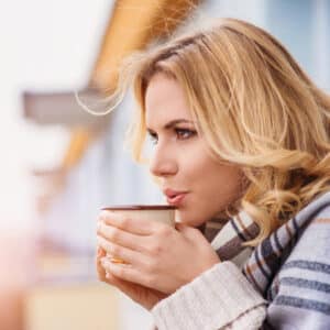 Frau sitzt mit Teetasse und Wolldecke am Strandhaus