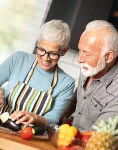 Zwei vitale Senioren (Frau und Mann) bereiten gemeinsam Gemüse und Obst in der Küche vor