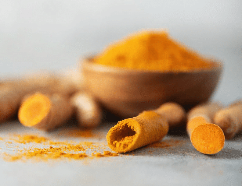 Holzschale mit Kurkuma-Pulver und aufgeschnittene Kurkuma-Wurzelknollen