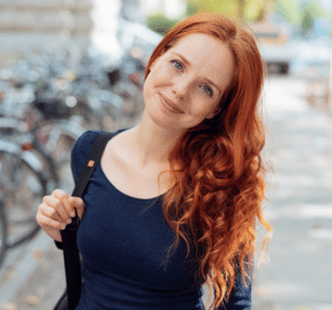 Junge Frau mit strahlend roten Haaren bei einem Stadtbummel zwischen Häusern und Fahrrädern