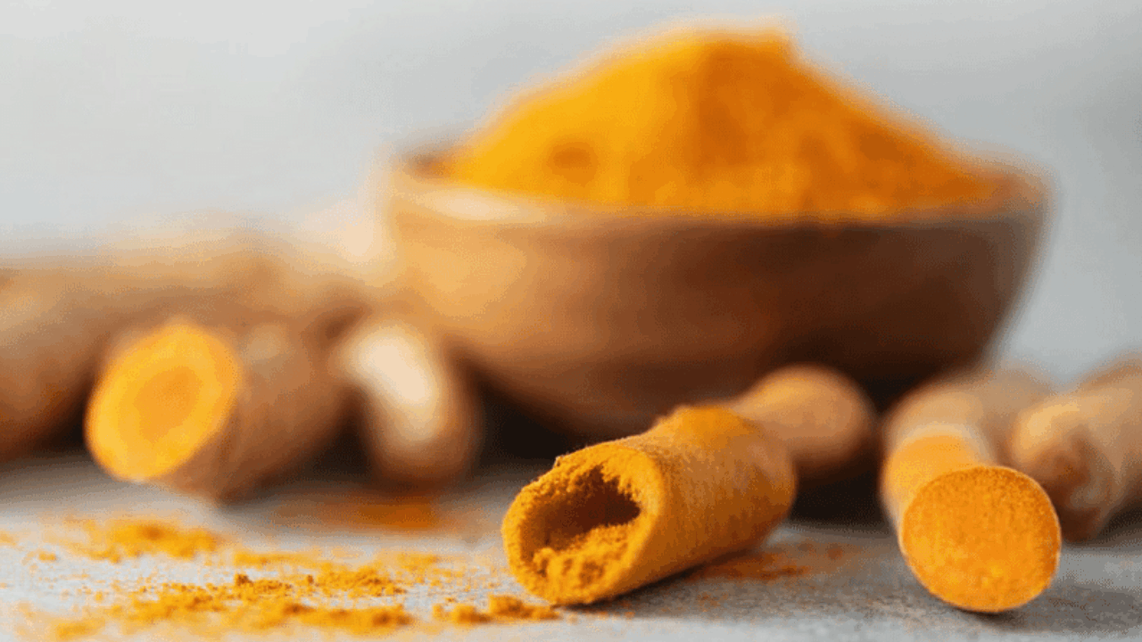 Holzschale mit Kurkuma-Pulver und aufgeschnittene Kurkuma-Wurzelknollen