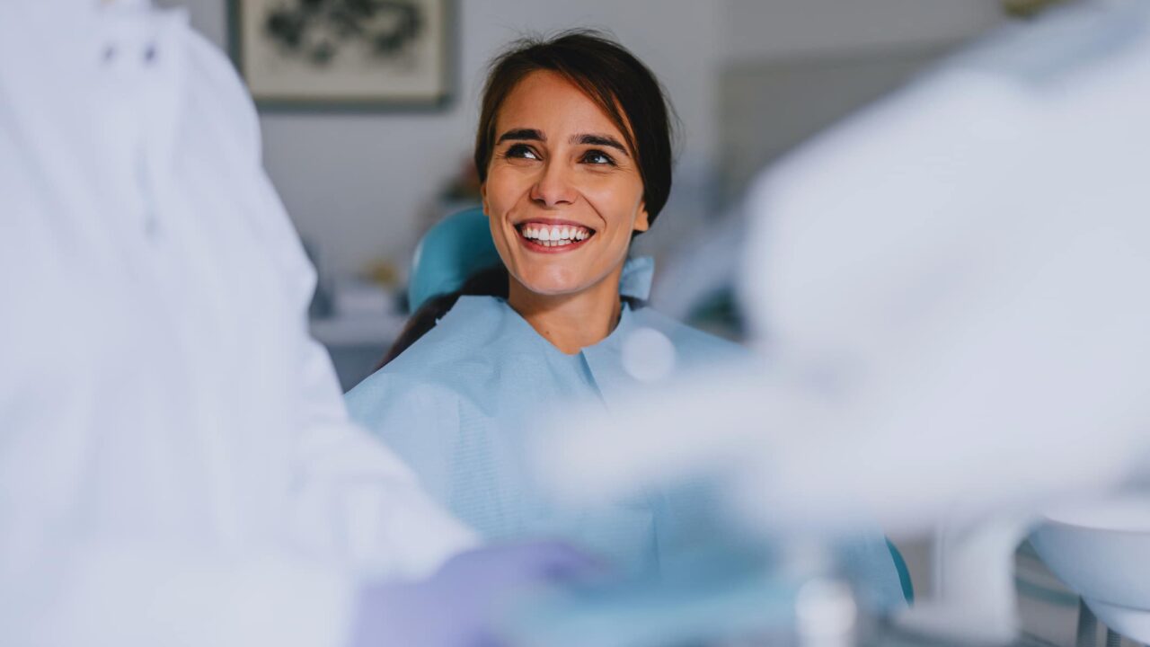 Smiling woman sitting in a dental chair interacting with a dentist during a checkup. Dentistry, healthcare, and patient care concepts.